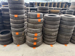 Stacks of secondhand 15" tyres with orange labels in a warehouse setting