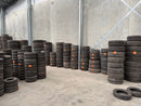 Stacks of secondhand tyres in a warehouse setting with concrete walls and floor.