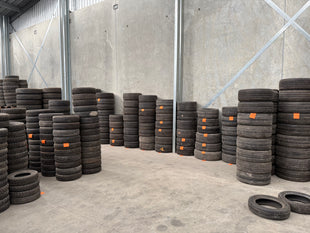 Stacks of secondhand tyres in a warehouse setting with concrete walls and floor.